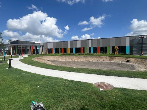 The colorful exterior of the Kids' Meals ExxonMobil Campus, with a curved sidewalk and open green space under a bright blue sky.